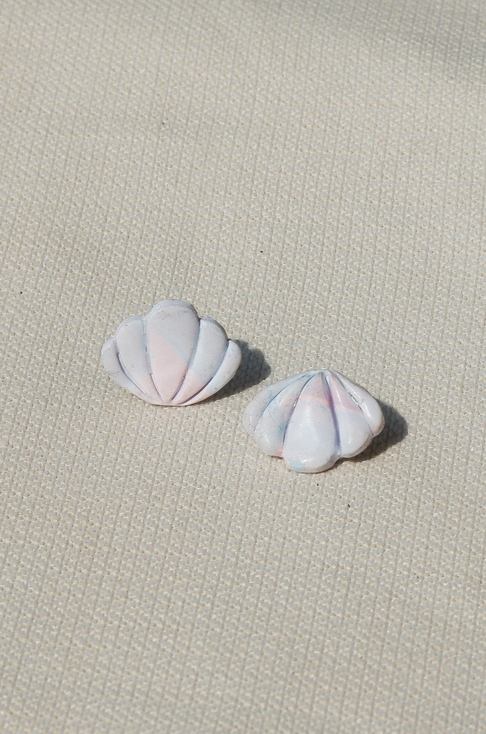 Pair of pink- blue - white shell-shaped earrings on a textured beige surface
