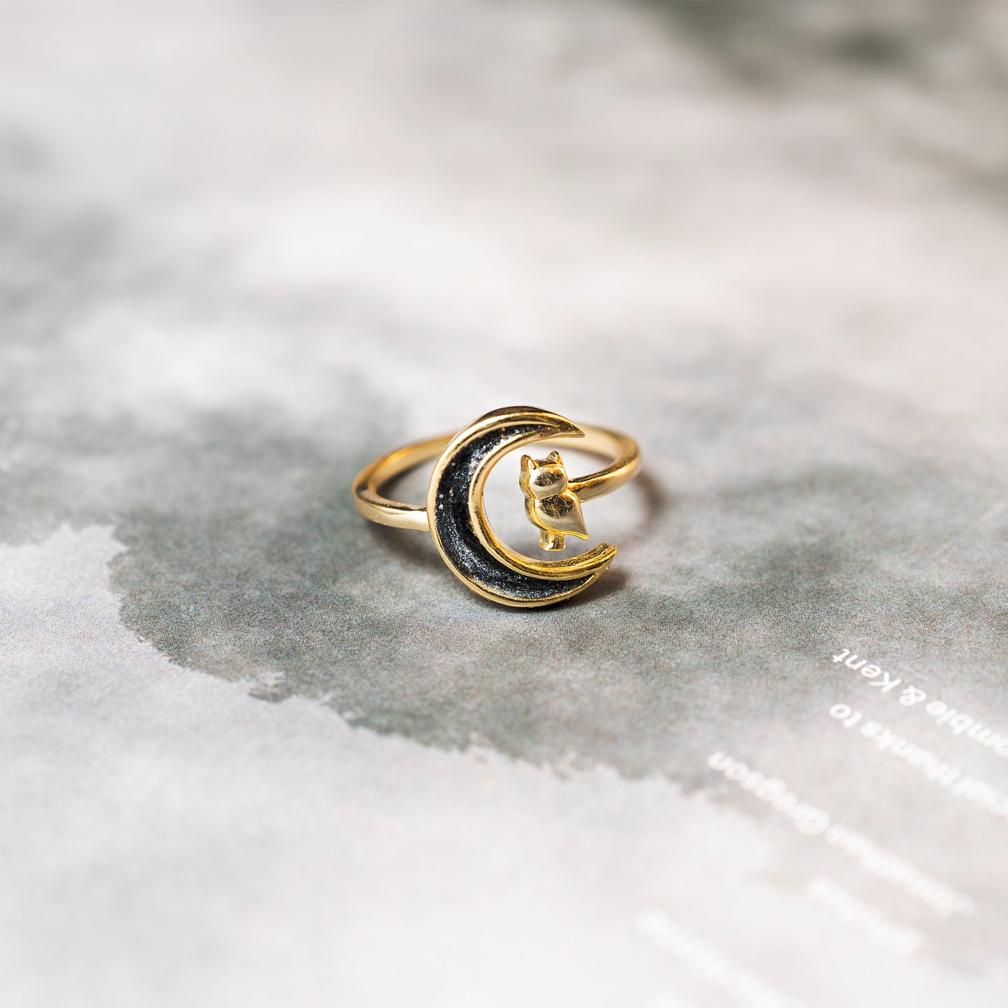 Gold and black moon-shaped ring on a textured surface