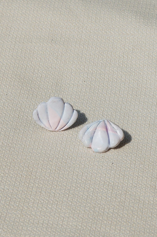 Pair of pink- blue - white shell-shaped earrings on a textured beige surface