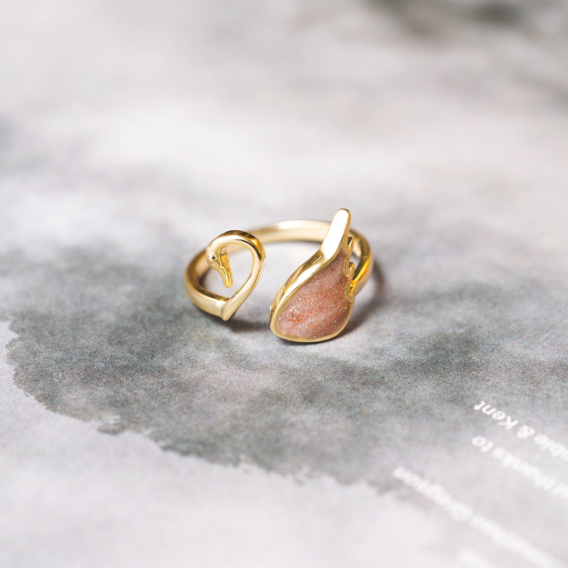 Gold ring with a heart design and red stone on a textured gray surface